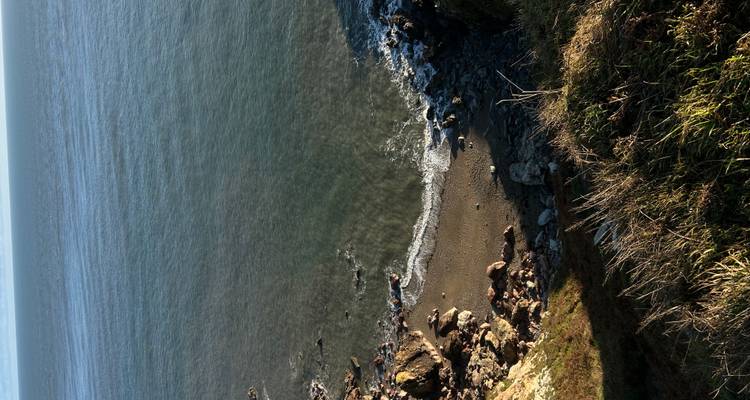 Secluded pebble beach at the base of rugged cliffs with calm blue sea beyond.