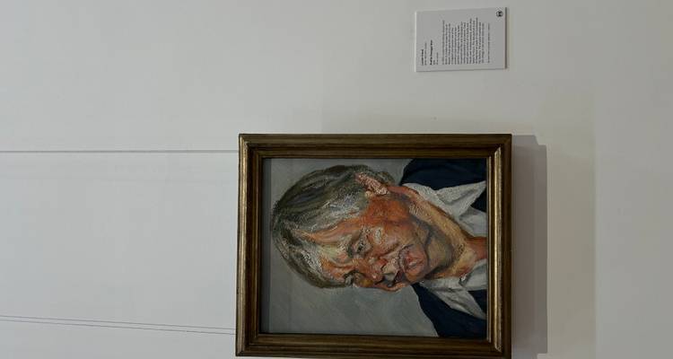 Portrait oil painting of an older woman displayed on a minimalist white gallery wall with description plaque.