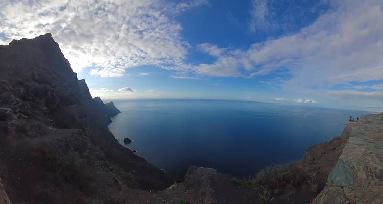 Des falaises volcaniques abruptes plongeant dans un océan bleu profond sous un ciel partiellement nuageux.