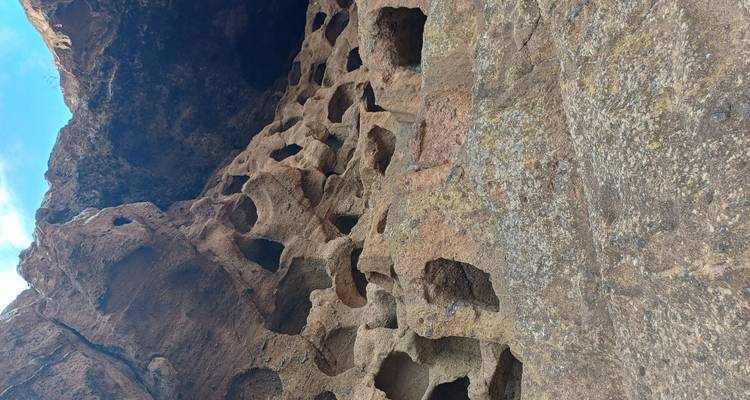 Paroi rocheuse présentant de nombreuses ouvertures carrées et rondes érodées sous un ciel bleu.