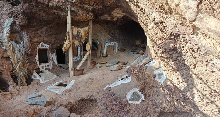 Intérieur d'une petite habitation de type caverneux avec des poteries faites à la main, des peaux d'animaux et des ouvertures peintes.