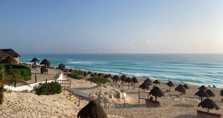 Vue panoramique de la plage publique de Cancun avec des rangées de parasols palapa et des vagues turquoise à l'aube