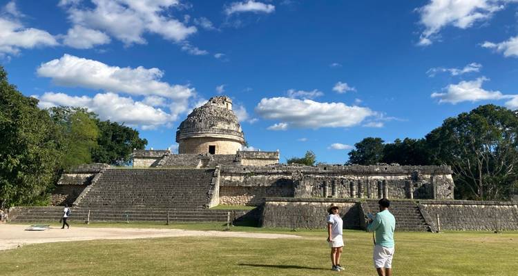 Ruines d'observatoire maya avec structure de dôme en pierre sous un ciel bleu, visiteurs se tenant sur la cour gazonnée