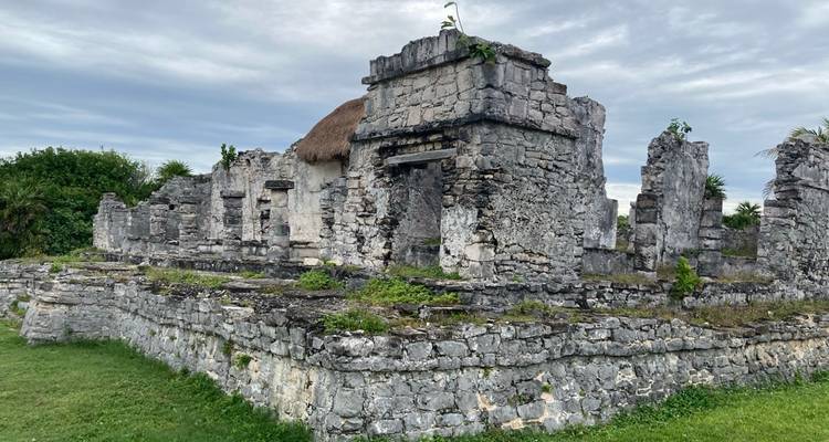 Ruines de pierre d'un ancien bâtiment maya côtier entouré de pelouse et de ciel nuageux
