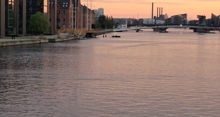 Vue répétée du canal de Copenhague au coucher du soleil avec skyline industrielle et eaux calmes.