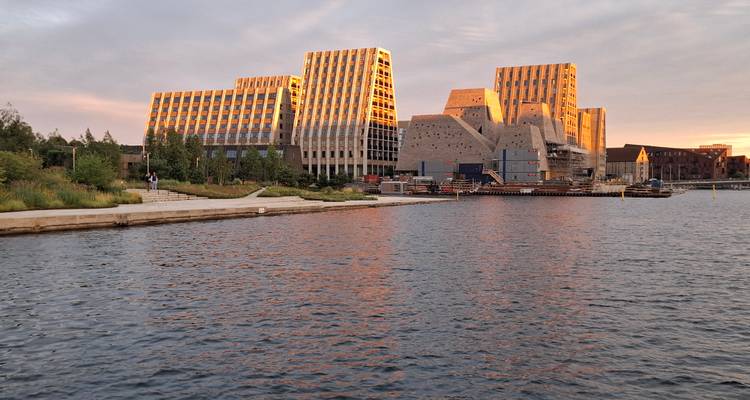 Les bâtiments modernes du campus en bord de mer brillent à la lumière dorée du coucher de soleil, reflétés dans le port de Copenhague.