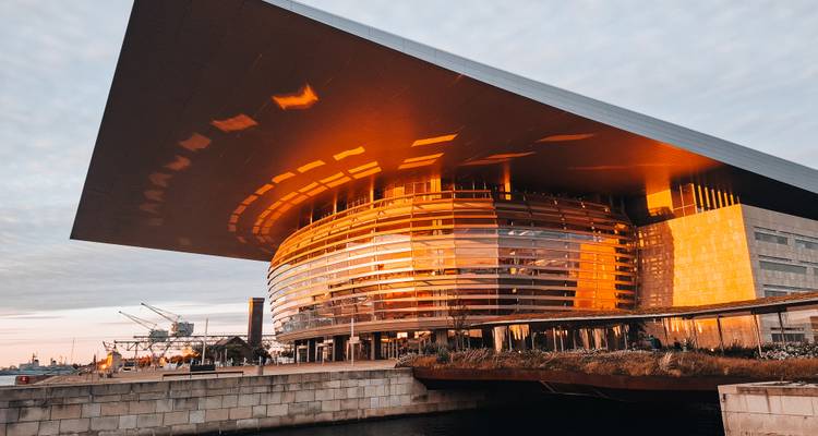 Casa de ópera circular moderna que brilla con reflejos dorados del atardecer junto a un canal.