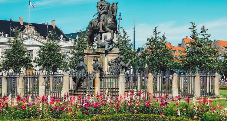 Estatua ecuestre de bronce rodeada de arriates de flores y barandillas de hierro en un parque urbano bien cuidado.