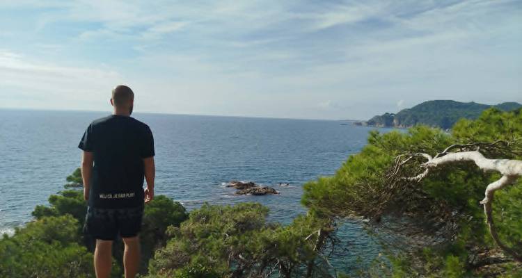 Un homme se tenant au bord d'une falaise regardant vers la Méditerranée bleue et la côte lointaine.