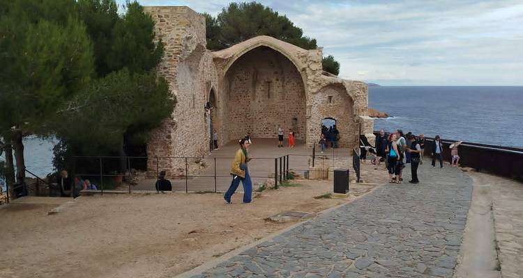 Des touristes explorant une ruine de chapelle en pierre perchée sur un sentier côtier falaisien.