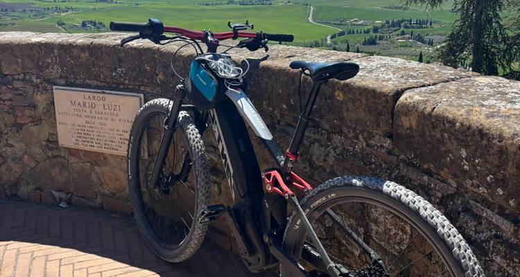 Vélo de montagne électrique garé contre un mur en pierre surplombant la vallée verte de Val d'Orcia