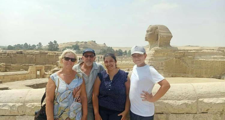 Un petit groupe posant devant le Grand Sphinx avec le désert brumeux et les ruines de pyramides en arrière-plan.