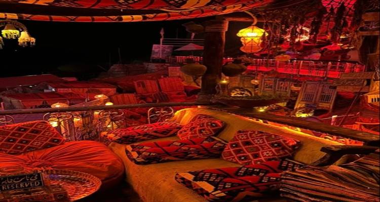 Acogedor lounge en la azotea decorado con cojines estampados, linternas e iluminación roja cálida por la noche.