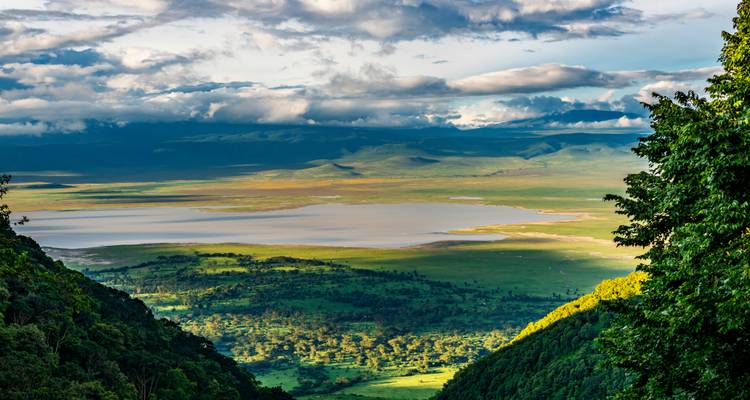 Epic panorama hacia el inmenso Cráter de Ngorongoro con lago y llanuras de retazos iluminadas por una luz dramática.