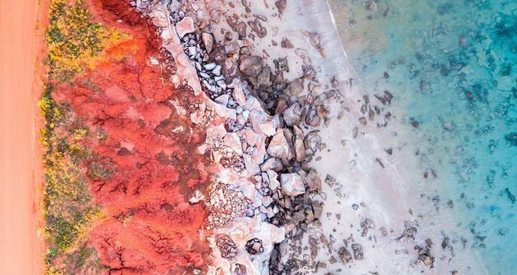 Vista aérea de acantilados rojo intenso bordeando una playa de arena blanca y un océano turquesa cristalino en la costa de Kimberley de Australia.