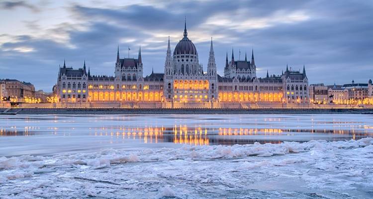 Le Parlement hongrois illuminé se reflète sur le Danube glacé à l'aube.