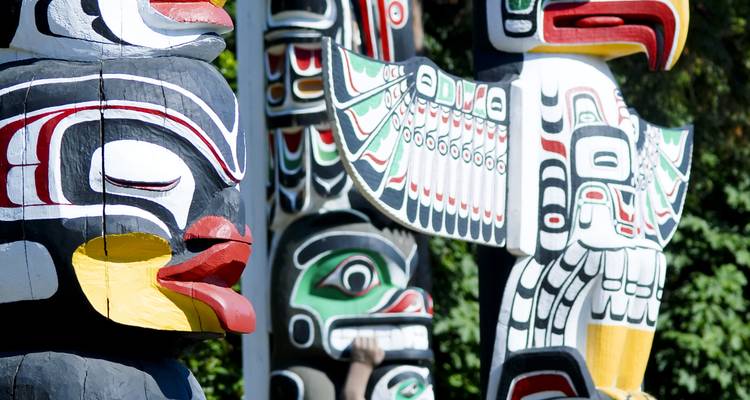 Colorful carved First Nations totem poles showcasing intricate patterns and animal figures set against greenery.