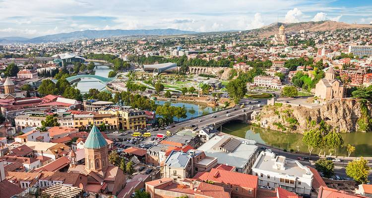 Panoramablick auf die Stadtlandschaft von Tiflis mit Fluss, Brücken und historischen Stadtvierteln an einem sonnigen Tag.