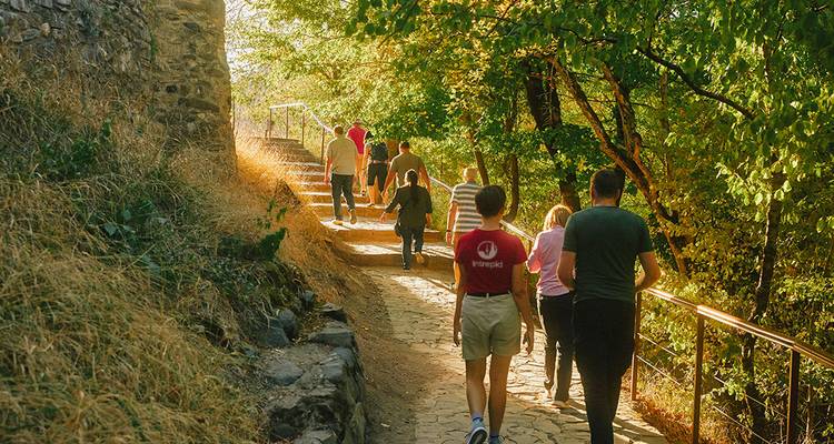 Reisende, die einen Kopfsteinpflasterweg neben antiken Steinmauern und Herbstbäumen hinaufgehen.