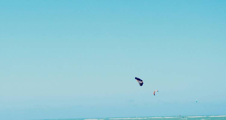 Scène minimaliste de ciel et de mer avec deux kitesurfeurs au loin sur des eaux turquoise