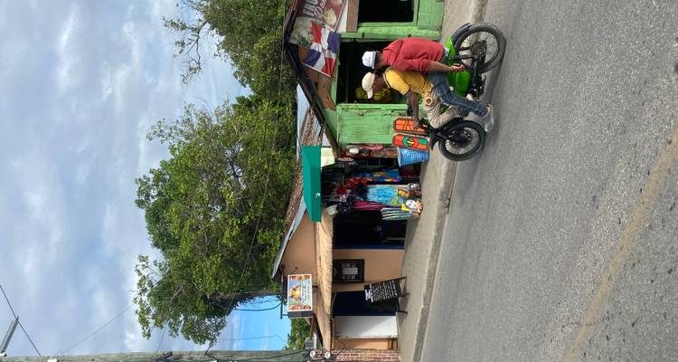 Deux motocyclistes passant devant des étalages routiers colorés et de petites boutiques en bois vert.