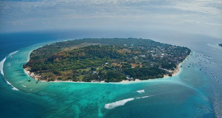 Panorama aérien impressionnant d'une île tropicale circulaire entourée de mers turquoise et de récifs.