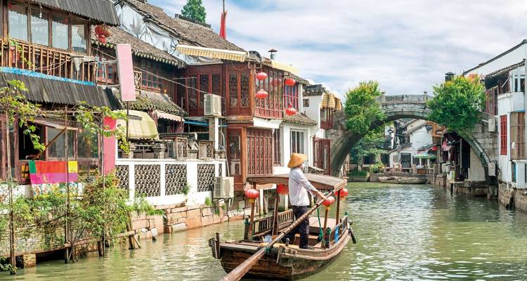 Traditionelles Holzboot, das durch einen engen Kanal gleitet, der von alten Häusern und roten Laternen in einer chinesischen Wasserstadt gesäumt ist.