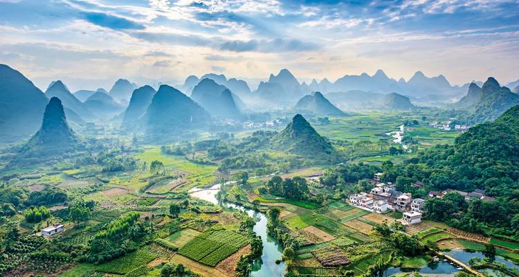Luftaufnahme eines nebelverhüllten Karstgebirges, eines mosaikartigen Reisfeldes und gewundener Flüsse in der Landschaft von Yangshuo.