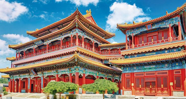 Lebhaft bemalte Hallen und reich verzierte Dächer eines kaiserlichen Palastkomplexes unter klarem blauem Himmel über Peking.