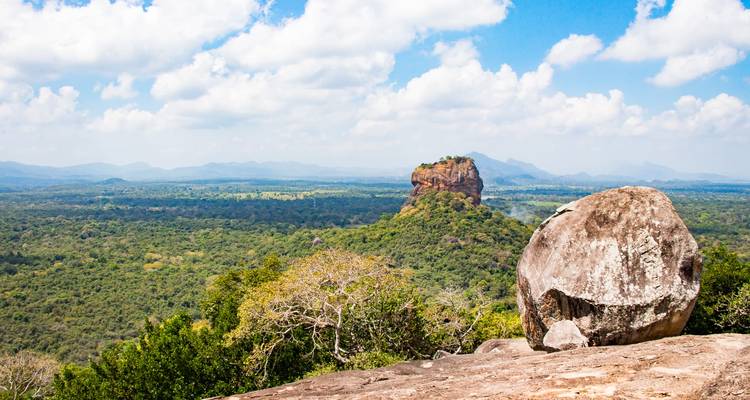 Iconic Sigiriya Rock die hoog boven het dichte bos uittorent, gezien vanaf een rotsachtig uitkijkpunt onder een heldere hemel.
