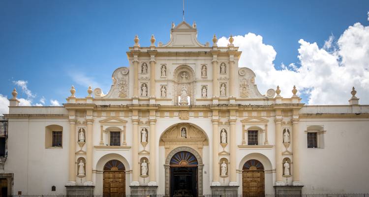 Fachada barroca pálida de la catedral de Antigua enmarcada contra un cielo azul brillante con nubes esponjosas.