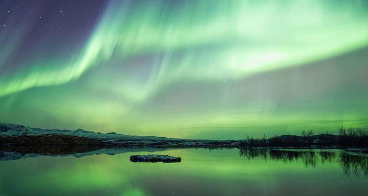 Las auroras boreales de un verde vibrante bailan en el cielo nocturno reflejadas en un lago tranquilo.