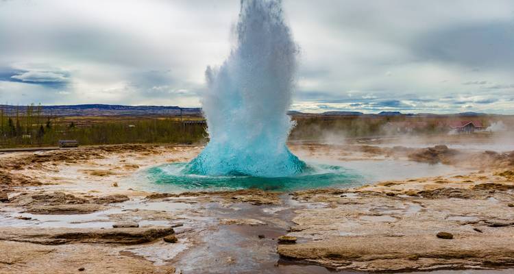 El géiser Strokkur estallando y disparando agua azul hacia el cielo en el área geotérmica de Geysir