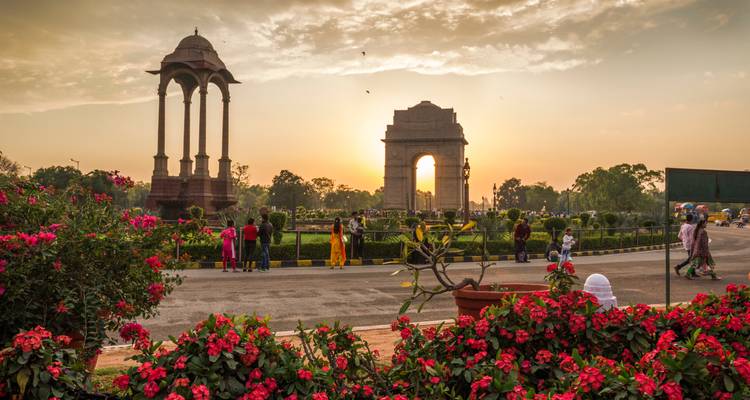 Das India Gate Denkmal, umgeben von Gärten und Besuchern, während eines warmen Sonnenuntergangs in Delhi.