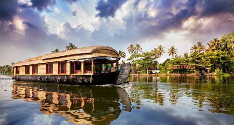 Traditionelle Hausbootfahrt aus Holz durch ruhige, spiegelglatte Gewässer der Backwaters von Kerala unter dramatischen Wolken.