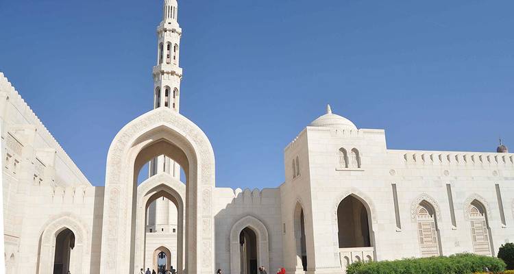 Weiße Marmorbögen und Minarett der Großmoschee Sultan Qabus unter einem tiefblauen Himmel.