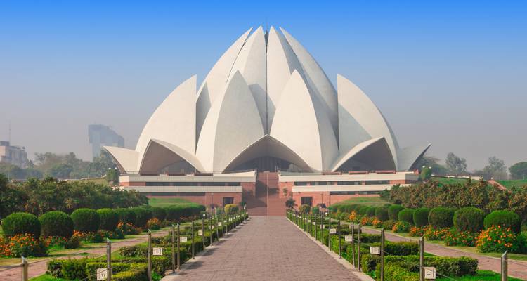 El Templo Baháʼí blanco con forma de loto se alza simétricamente al final de un camino bien cuidado bajo un cielo radiante.