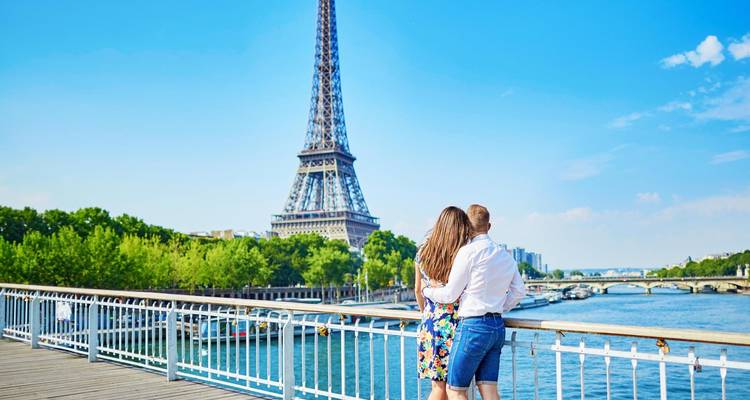Jeune couple s'embrassant sur un pont surplombant la Seine avec la tour Eiffel clairement visible.