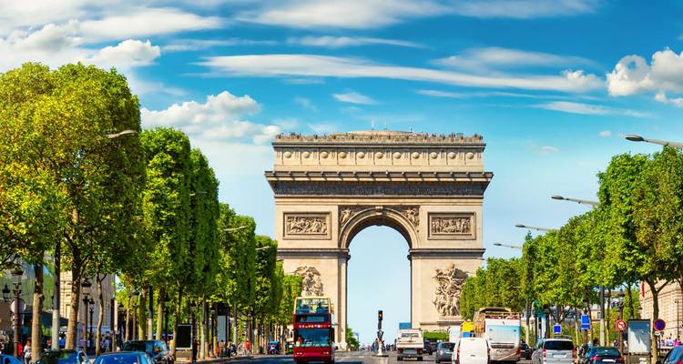 Arc de Triomphe se dressant au-dessus d'une avenue animée sous un ciel bleu éclatant.