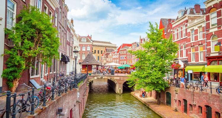 Kleurrijke cafés en fietsen sieren een charmant kanaal in Utrecht onder een heldere zomerhemel.