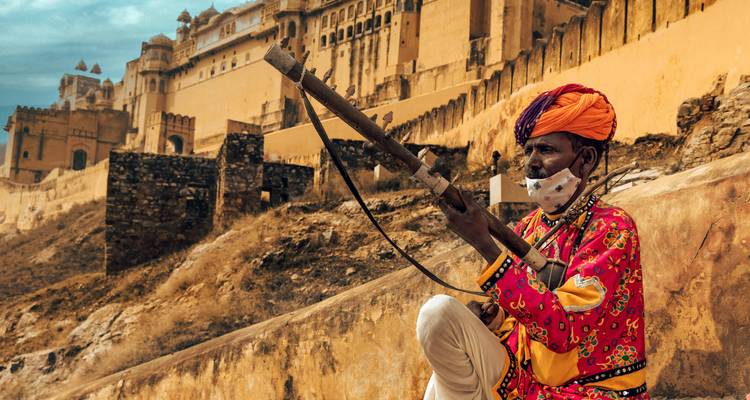Un garde vêtu de manière traditionnelle avec un mousquet est assis contre les murs ocre du Fort d'Amber sous un ciel dramatique.