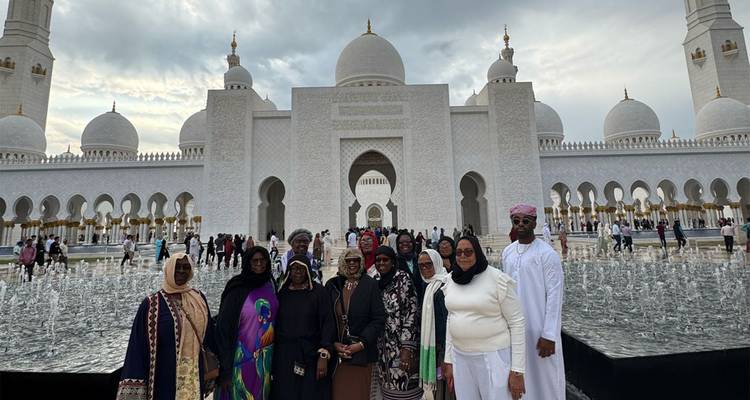 Un grand groupe de touristes se tient devant la façade ornée de la Grande Mosquée Sheikh Zayed sous un ciel chargé.
