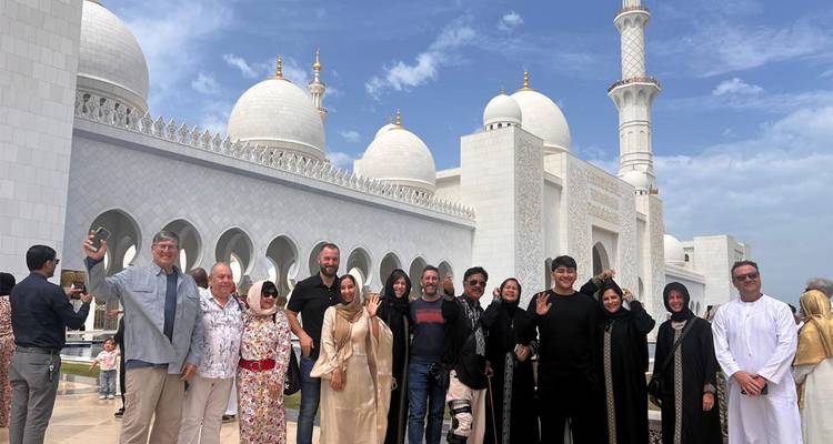 Les touristes vêtus d'abayas traditionnelles sourient et font des gestes de la main à l'extérieur des colonnades de la Grande Mosquée du Cheikh Zayed.