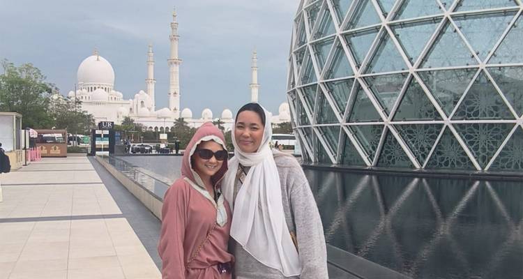 Deux femmes posent à côté du dôme en verre géométrique et du bassin réfléchissant à l'extérieur du complexe des visiteurs de la Grande Mosquée Sheikh Zayed.