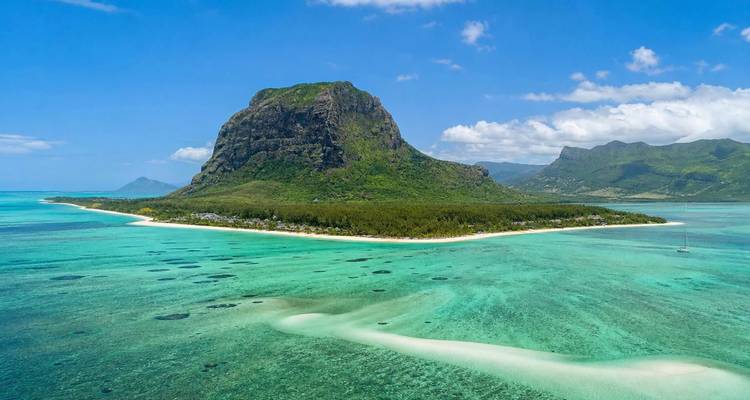 Clear turquoise waters surrounding Le Morne peninsula with its iconic basalt mountain under blue skies.