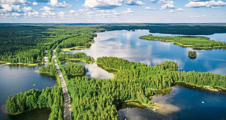 Hochaufnahme von waldgesäumten Seen, die durch eine schmale Brücke in Finnlands Region Saimaa an einem sonnigen Tag verbunden sind.