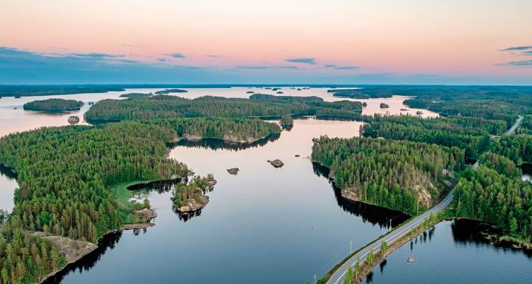 Sanfte pastellfarbene Dämmerung über Inseln und ruhigem Wasser des Saimaa-Sees mit einer sich windenden Straße durch den Wald.