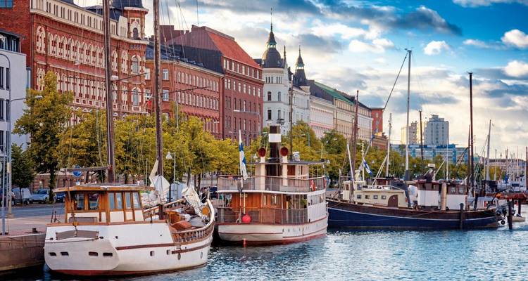 Historische Boote, die in Helsinkis eleganter Hafenanlage vertäut sind und von aufwendigen Backstein- und Steingebäuden umgeben sind.