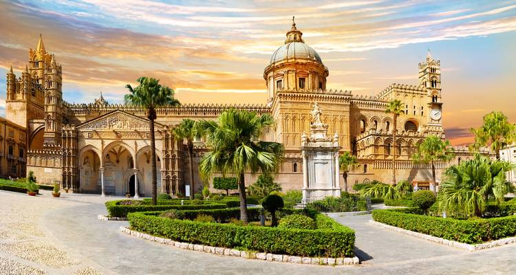Der Palermo Dom, erleuchtet von goldenem Sonnenuntergangslicht, mit palmengesäumten Gärten im Vordergrund.