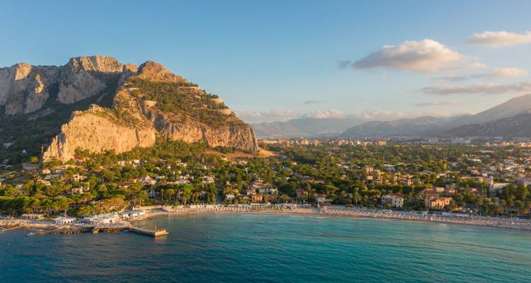 Malerische Bucht mit türkisfarbenem Wasser, Sandstrand und steilen Bergen, die sich hinter einer Küstenstadt erheben.